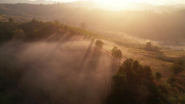 The rays of the sun shine through the clouds into the misty sea above the mountains in the morning. 4K aerial shot on sunrise
