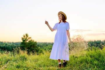 Naklejka na ściany i meble Beautiful woman in white dress hat with bouquet of flowers on meadow, in sunset