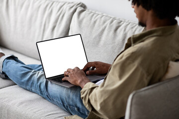 Black Man Using Laptop Computer With Blank Screen While Sitting On Couch