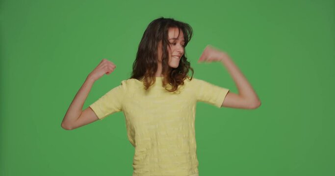 Cool funny young girl showing biceps, make muscles gesture, raising hands on chromakey background. Personal achievements