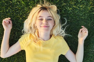 Top view of a beautiful teenage blonde lying on the green grass.