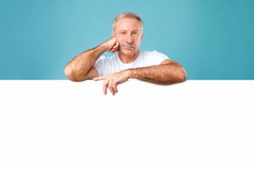 Mature man peeking out blank white advertising billboard at studio