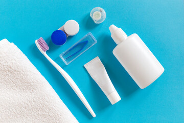 Flatlay of dental care tools and lenses: toothbrush and paste, container and towel on a blue background. Morning routine and everyday hygiene concept