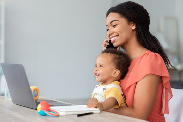 Black Woman Talking On Cellphone And Using Laptop With Baby On Hands