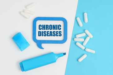On a white and blue table are pills, a marker and a blue plaque with the inscription - CHRONIC DISEASES