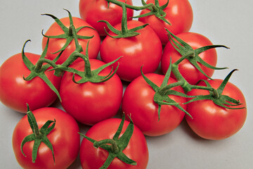 Tomates  maduros com os ramos verdes em fundo neutro.