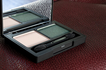 Decorative cosmetics. Eye shadow in palette with applicator and mirror on burgundy leather background