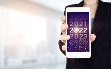 Concept Start New Year 2022. Hand hold white smartphone with digital hologram 2022 sign on light blurred background. Concept for vision 2021-2022. Businessman welcome year 2022.