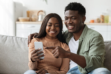Happy black lovers using smartphone together, home interior