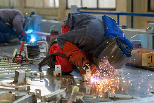 Two Welders With Torch And Welding Sparks Of Molten Metal. Workers With Welding Helmet And Protective Workwear Welding Train Construction At The Train Factory. 