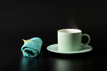  A mint-colored cup with a hot drink and a napkin on a black background. A haze of steam rises above the cup. Copy space.
