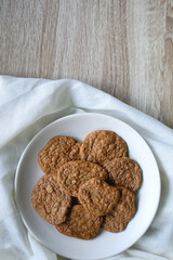 Plate of healthy, gluten free and high protein cookies, made with bananas, eggs, chia seeds and almonds. White tablecloth and wooden background. Flat lay. 