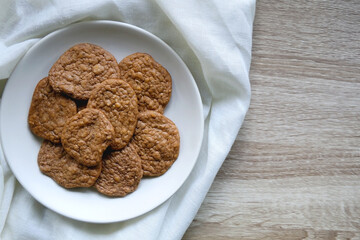 Plate of healthy, gluten free and high protein cookies, made with bananas, eggs, chia seeds and almonds. White tablecloth and wooden background. Flat lay. 