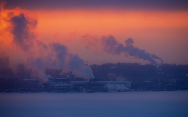 Chimneys smoke in winter against the background of the city and the sky.