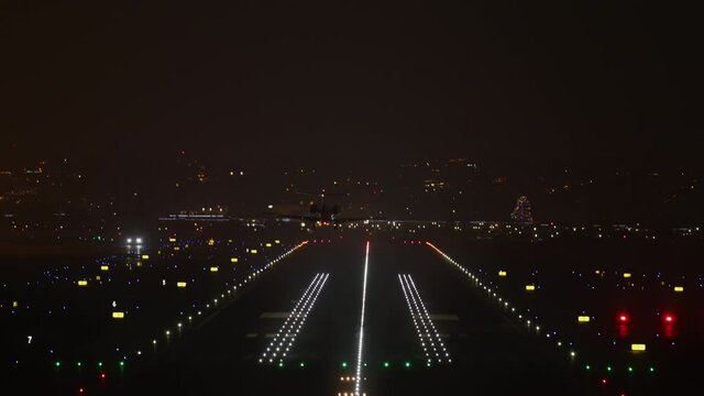 Huge passenger airliner arriving along single runway, lit by colorful lighting. Aircraft landing to the city airport as seen from the terminal. High quality 4k footage