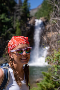 Cute woman hiker with braided hair wearing a tank top poses at Running Eagle Falls waterfall in Glacier National Park