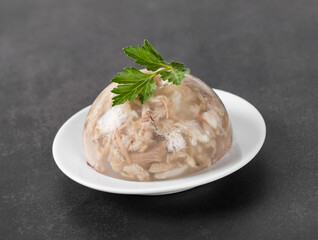 Cold appetizer. Pork jelly with pieces of meat with parsley on a plate on a dark gray background