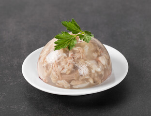 Traditional Russian festive cold appetizer. Pork jelly with pieces of meat with parsley on a plate on a dark background