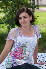 Naklejka premium A girl in a knitted blouse sits on a plaid in the park. Camping on a sunny day. 