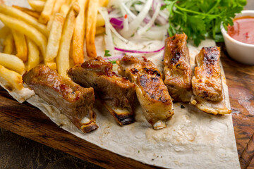 Kebab from lamb ribs with french fries, red onion and tomato sauce on the board close up