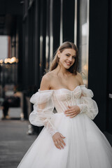 Portrait of beautiful happy girl with long hair in white wedding dress on the city background....