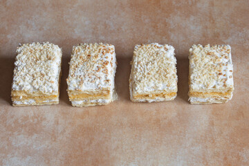 A row of individual servings of Millefeuille made with puff pastry and filled with pastry cream and meringue with toasted chopped almonds and icing sugar on abstract background. Traditional sweets.