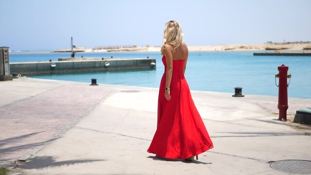 beautiful blond female model in long red cocktail dress walking for invitation in slow motion