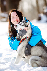 Girl with a cute husky in a winter park. Dog playing in the snowy forest