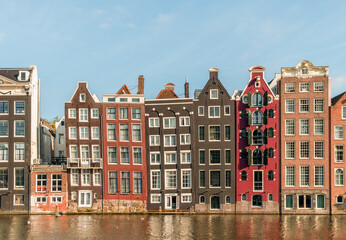 Typical Dutch Amsterdam houses at the Amsterdam canal Damrak on a sunny day, Holland, Netherlands. - obrazy, fototapety, plakaty