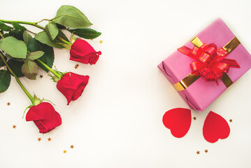 Pink gift box with gold ribbon and two hearts, bouquet of red roses on white background. Valentine's Day, wedding, mother's day, birthday. Postcard. Flat lay.