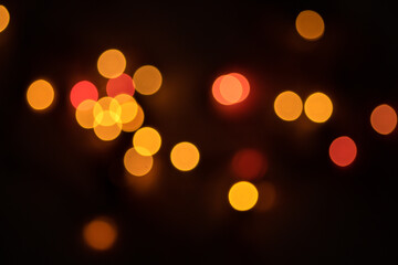 Defocused bokeh lights on black background, an abstract naturally blurred backdrop for Christmas eve or birthday party. Festive light texture. Yellow and red garland in blur. Overlay effect for design