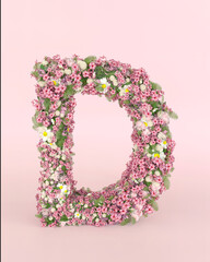 Creative letter D concept made of frash Spring wedding flowers. Flower font concept on pastel pink background.