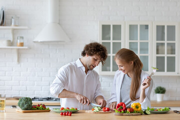 Happy couple is preparing healthy food on light kitchen. Cooking together salad