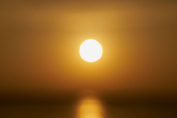 A blurry sun rising over the sea at dawn.