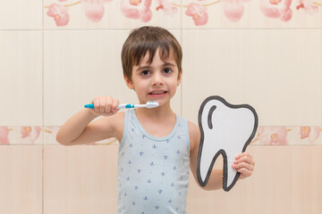 A little boy is brushing his teeth, holding a cardboard tooth in his hands. Oral hygiene.