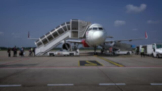 Blurred defocused people boarding low cost airplane at International Airport on outside platform at a sunny day. Travelers plane outdoors hot weather