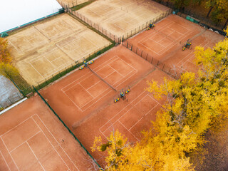Fly above orange clay tennis courts in city park. Vivid yellow autumn trees near sports recreation area. Aerial treetop view on colorful Kharkiv, travel Ukraine