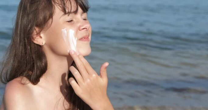 Child face with sunscreen. A happy young girl apply sunblock on her face on the sunny beach.