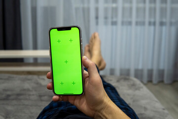 Faceless man lying on sofa with smartphone in hand with green screen. Man reading on the phone