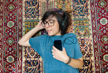 Pleasure of listening music, teen girl colored hairs big glasses headphones lying down on a carpet