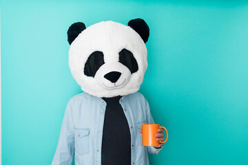 Person in panda mask holding a cup of coffee on colored background. Happy lifestyle concept