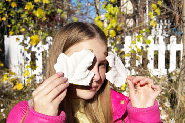 A blonde teenage girl closes her eye with an autumn poplar leaf
