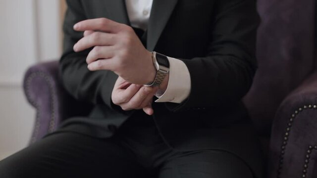 Man in suit put on old-fashioned wrist watch. Groom dresses. Handsome male businessman waiting for meeting. Hand with clock close-up. Waits. Looks at clock, time. Wristwatch on man arm. Slow motion