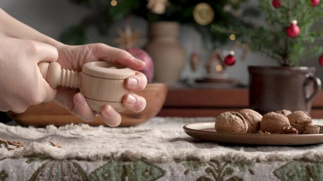 Hands cracking walnuts with a nutcracker, with a decorated Christmas tree in the background