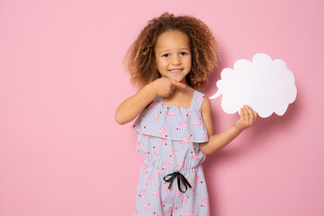 Smiling little girl in summer clothes showing paper cloud standing isolated over pink background.