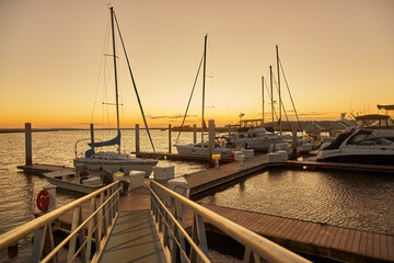 Walking down the pier to boats docked under low light at sunset - Powered by Adobe