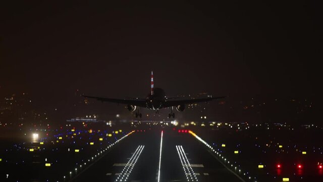 Scenic view of colorful illumination along the runway at night. Big passenger airliner landing at night with a cityscape in the background. High quality 4k footage