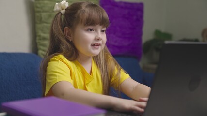little child does homework on a laptop, a girl types on a keyboard, home school on a computer online, learning a kid remotely at home, playing games in computer application program, modern technology
