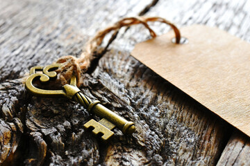 A close up image of a vintage brass key tied to a brown paper label on an old wooden desk top. 