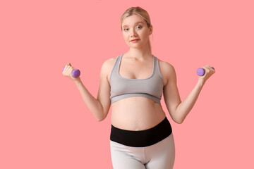 Sporty young pregnant woman with dumbbells on pink background